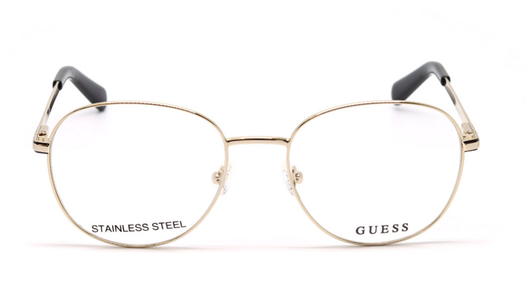 Gold metal eyeglass frames with clear lenses, featuring the GUESS brand name and STAINLESS STEEL text on the lower rims, with black temple tips, shown against a plain white background.