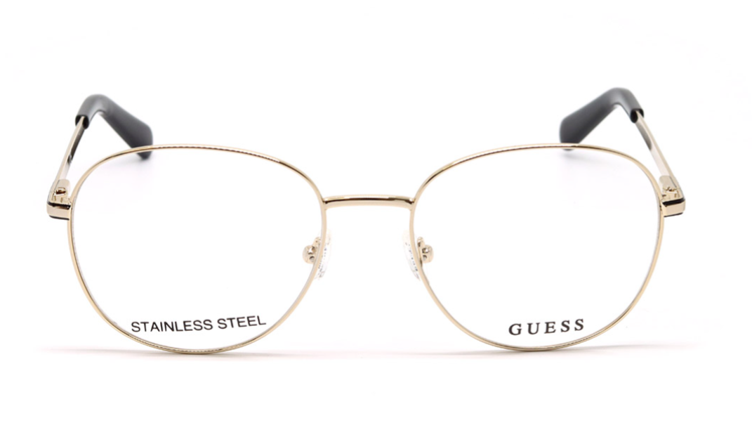 Gold metal eyeglass frames with clear lenses, featuring the GUESS brand name and STAINLESS STEEL text on the lower rims, with black temple tips, shown against a plain white background.
