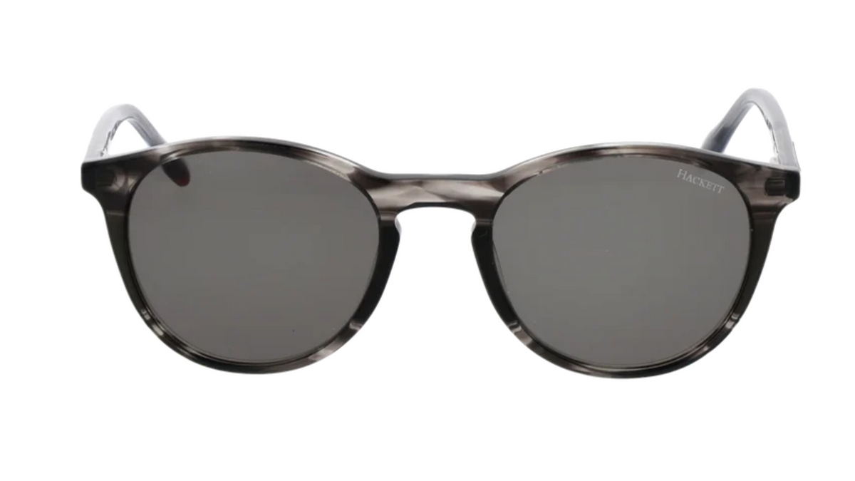 A pair of round-frame sunglasses with a translucent dark gray and black tortoiseshell pattern, dark gray lenses, and silver temple tips. 
