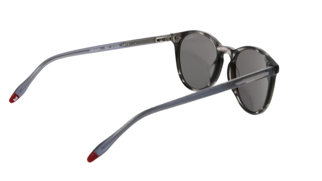 Round sunglasses with a smoky gray acetate frame, dark gray lenses, and red-accented temple tips, shown on a plain white background.